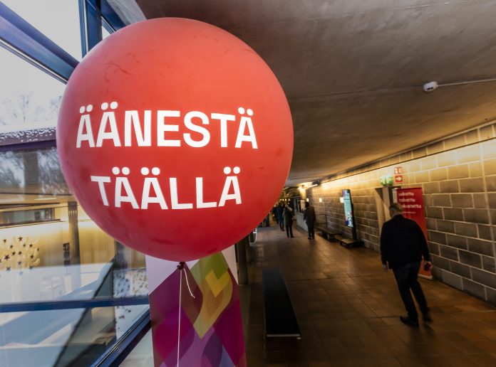 Seurakuntavaalien äänestys Espoossa Tapiolan kirkolla 20.11.2022 Suuri punainen ilmapallo, jossa lukee ”Äänestä täällä”, vaalipaikan käytävällä. Taustalla ihmiset kulkevat käytävää pitkin.
