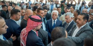 Palestiinalaishuiviin pukeutunut prinssi seisoo väkijoukossa ja kättelee ihmisiä.