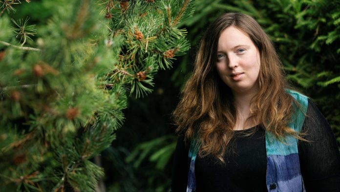 Amanda Nylund00001 by Jani Laukkanen Puolilähikuvassa on nuori, pitkähiuksinen nainen männyn edessä.