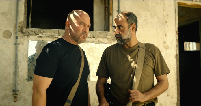 Fauda Lior Raz as Doron Kavillio_ Yaakov Zada-Daniel as Eli copy korjattu Kaksi aseistettua parrakasta israelilaista sotilasta seisoo vaalean rapatun rakennuksen edessä.