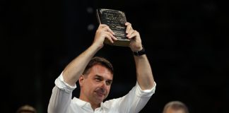Senaattori Flávio Bolsonaro vaalitilaisuudessa valkoinen paita päällään, pitämässä käsissään Raamattua korkealle kohotettuna