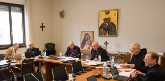Pappismiehiä tummissa asuissaan kokoontuneina pöydän ympärille teologisiin keskusteluihin Roomassa.