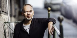 Politiikan kulisseissa työskennellyt Markus Österlund vaihtoi uransa pastorin työhön Harmaapartainen mies tummassa neuletakissa nojaa vihreään kaiteeseen ja katsoo kameraan kaupunkimaisemassa.