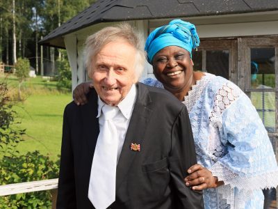 Kuvassa on vaaleaihoinen, harmaatukkainen mies tummassa puvussa ja kravatissa sekä tummaihoinen nainen jolla on turkoosi päähine. Molemmat hymyilevät iloisesti.