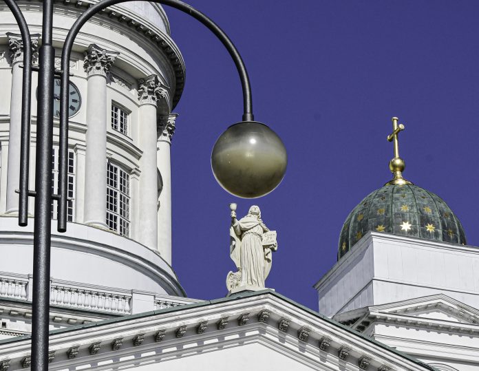 Tuomiokirkko_hki_pallo1_byOS Kuvassa Helsingin tuomiokirkon tornia, patsas ja pallon muotoinen valaisin sinistä taivasta vasten.
