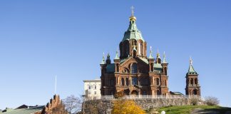 Ortodoksisen kirkon piispat: Ortodoksipappi ei saa osallistua papin roolissa samaa sukupuolta olevan parin vihkimiseen Helsingin Uspenskin katedraali kohoaa kallioisella kukkulalla kirkkaansinistä taivasta vasten. Punatiilistä ortodoksikirkkoa koristavat vihreät katot ja kullatut kupolit risteineen. Etualalla näkyy keltaiseksi värjäytyneitä syyspuita, katua ja pysäköityjä ajoneuvoja.