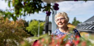 Kuvassa harmaahiuksinen silmälasipäinen nainen katsoo vasemmalle. Taustalla näkyy puita ja vettä.
